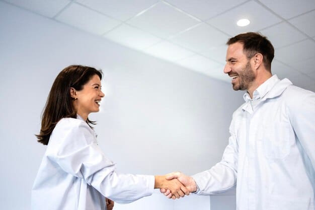 A close-up shot of two individuals at a biotech event, shaking hands with confident smiles. One person is handing over a business card. The background is slightly blurred, showing other attendees in professional attire.